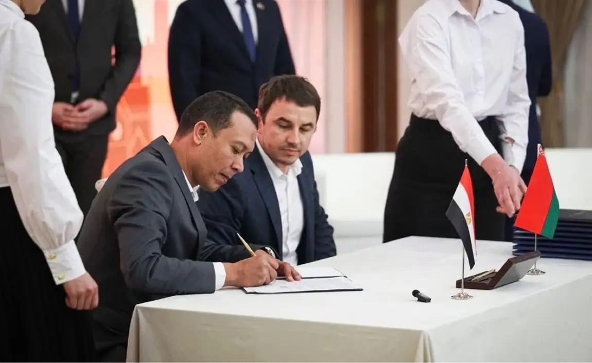 El-Adawy signing the agreement document, with Egyptian and Belarusian flags on the table